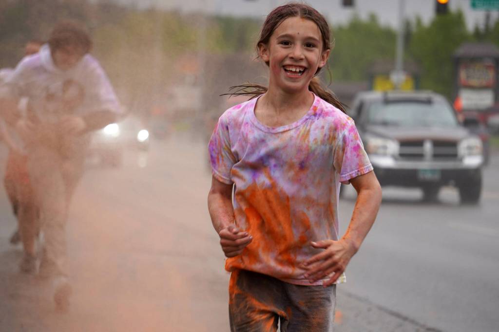 Emily Musgrove emerges from a cloud of orange powder during a color run as part of the opening night of the Levitt AMP Soldotna Music Series along the Sterling Highway in Soldotna, Alaska, on Wednesday, June 5, 2024. (Jake Dye/Peninsula Clarion)