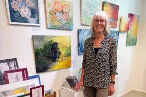 Artist Ingrid McKinstry stands next to her current mixed media exhibit and her work available year-round at Fireweed Gallery in Homer, Alaska. Photo provided by Ingrid McKinstry