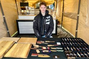Jaxon Bourne sits in his booth at the Homer Farmers Market with his handmade knives, pens and cutting boards on Saturday, Sept. 13, 2025, in Homer, Alaska. Photo by Christina Whiting