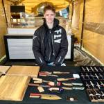 Jaxon Bourne sits in his booth at the Homer Farmers Market with his handmade knives, pens and cutting boards on Saturday, Sept. 13, 2025, in Homer, Alaska. Photo by Christina Whiting