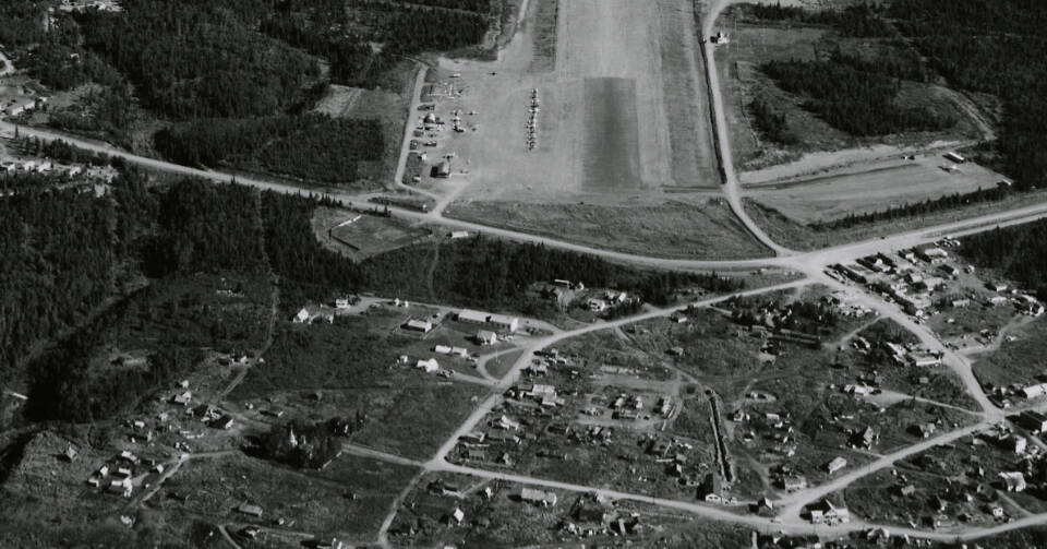 This 1960 aerial photograph from the Civil Aeronautics Administration shows, from top to bottom, the southern end of the Kenai Airport runway, the Spur Highway and the fledgling city of Kenai. Near the center of the photo is a cluster of white-painted buildings then owned by the U.S. Fish & Wildlife Service, which managed the Kenai National Moose Range. Enclosed in a small group of trees south-southwest of these buildings is the Russian Orthodox Church.