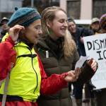 Event organizers Laura Stats, left, and Ariel Hasse-Zamudio sing lyrics off a page to an original song by Eric Antrim, a local musician and Forest Service employee. If we want to say, Dont forget Alex, now is the time, the crowd sang from pages with the lyrics. If we want to say we love our neighbors … now is the time.
