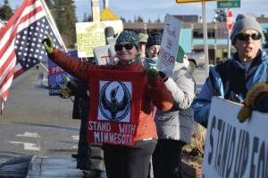 Jan Krehel waves at cars passing by as she holds a "Stand With Minnesota" banner during the "ICE OUT" demonstration on Sunday, Feb. 1, 2026, at WKFL Park in Homer, Alaska. (Delcenia Cosman/Homer News)